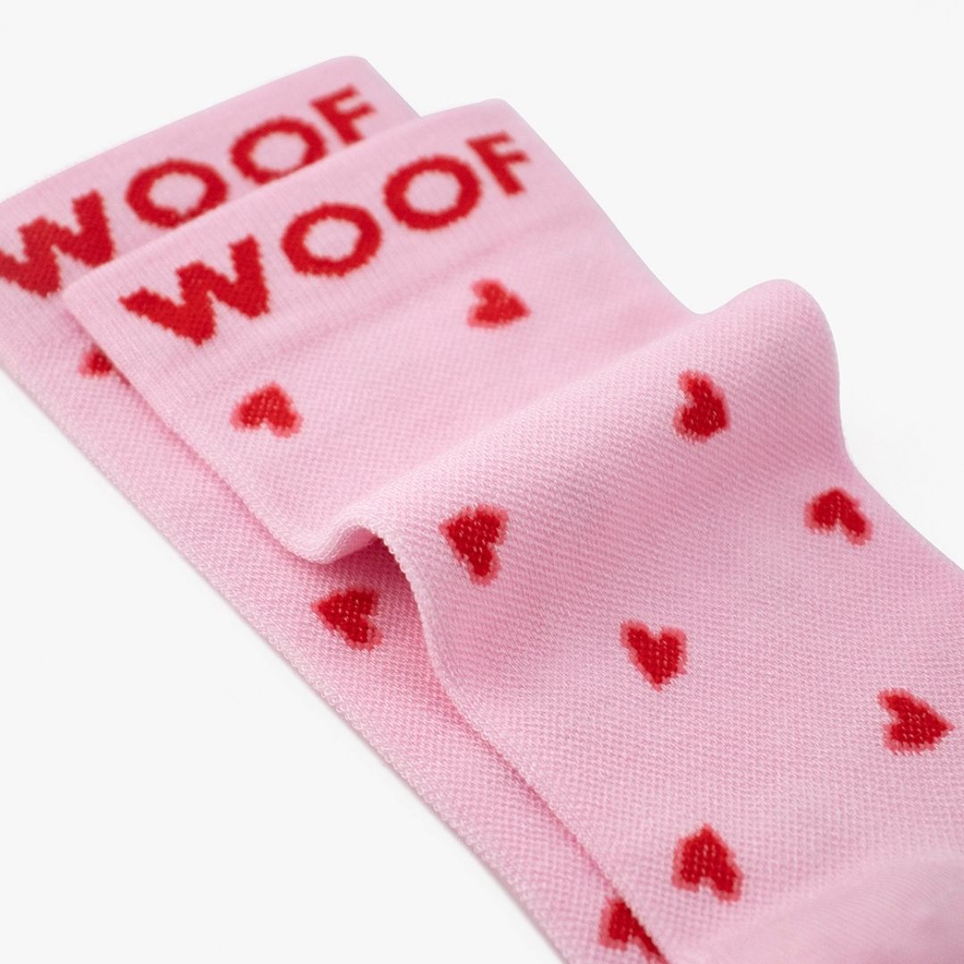 Macro close-up shot showing the Hearts Bamboo Crew Compression Socks folded neatly to highlight the red woven "WOOF" cuff bands and the red heart knit pattern layout.  