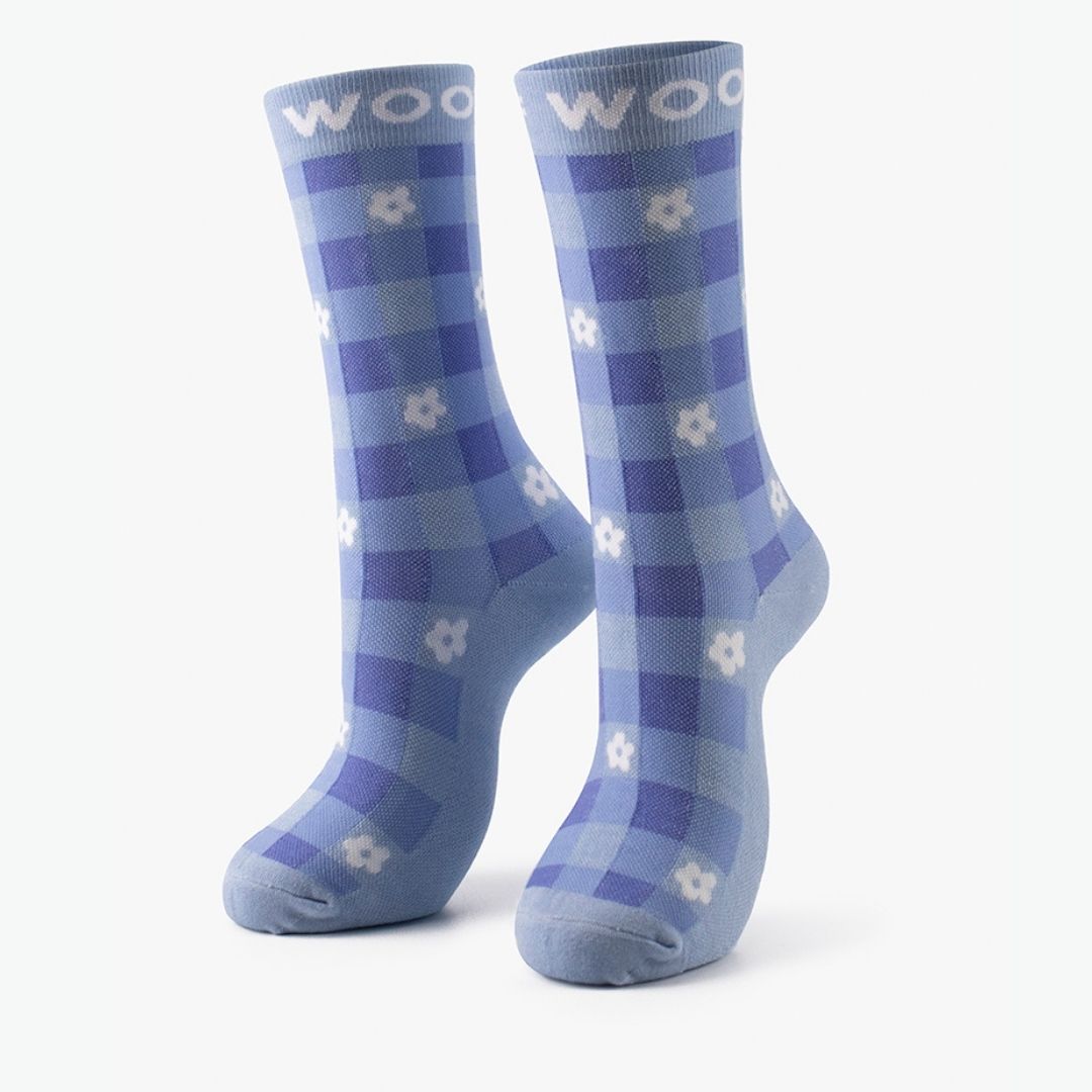 A pair of blue Floral Gingham Bamboo Crew Compression Socks standing upright, featuring a blue-and-light-blue check pattern with white daisy motifs and light blue "WOOF" woven into the top cuffs.  
